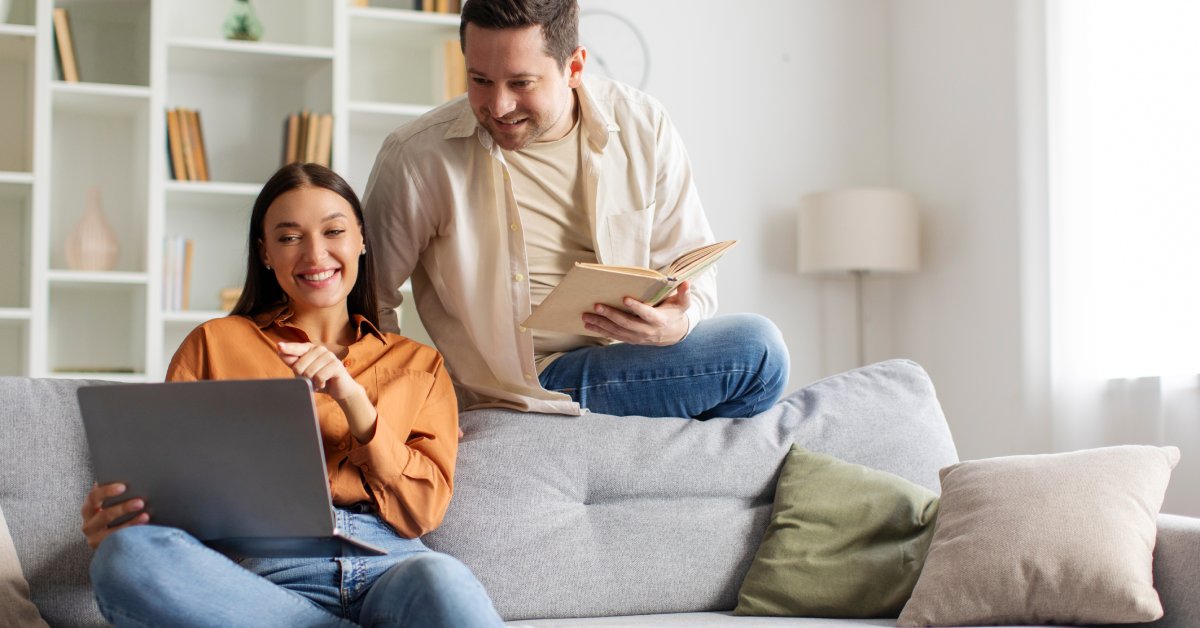A person sitting on a couch and pointing at a laptop screen. The person behind them looks at the screen.